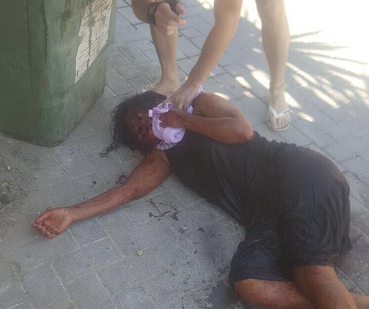 האישה מוטלת ברחוב, שניות אחרי הדקירה, עבורי אורח מנסים לעצור את הדימום (צילום: וואצאפ)
