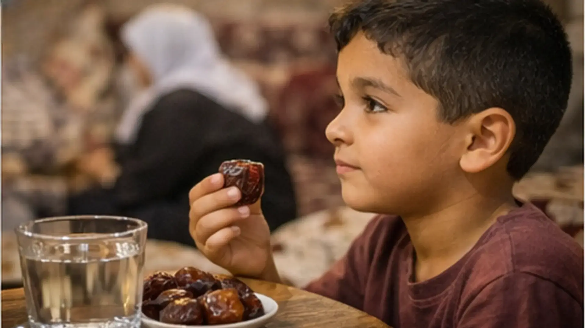 طفل يمسك تمرة بيده منتظراً الأذان بجانب عائلته