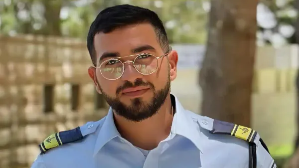 צילום דיוקן של לוחם היס''מ רן גואילי במדים, לצד נר זיכרון ודגל ישראל ברקע.