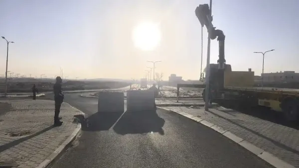 בטונדות בטון גדולות החוסמות כביש בכניסה ליישוב בדואי בנגב, לצד ניידות משטרה וכוחות הפועלים בשטח.