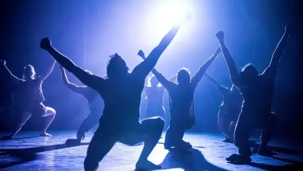 רקדני להקת המחול קמע מבצעים קטע מתוך היצירה Gray מאת תמיר גינץ על במה חשוכה עם תאורה דרמטית.