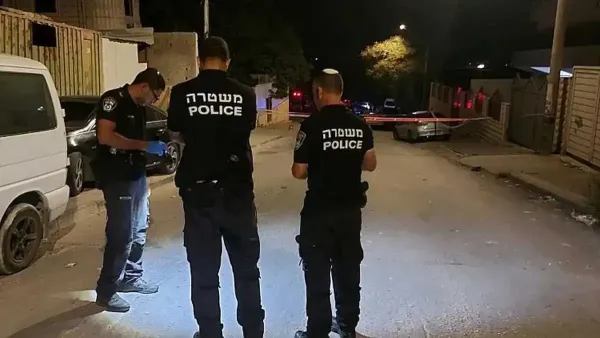 ניידות משטרה בכביש בכניסה ליישוב חורה בלילה, פנסי כחול-אדום דולקים, אווירה מתוחה.