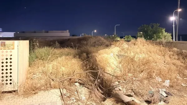 מגרש ריק בשכונת מגורים חדשה בבאר שבע עם עשבייה, פסולת בנייה ובתים מאוכלסים מסביב